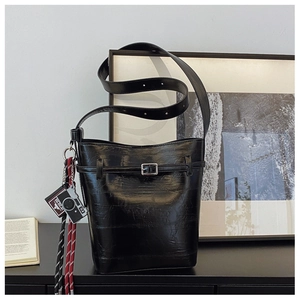 Detail of a black pleated bucket bag with silver buckles and a camera-shaped charm