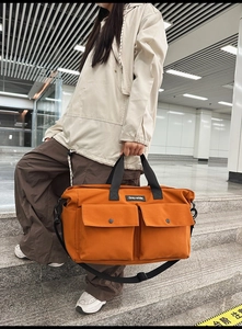 Macro detail of orange canvas tote bag featuring double flap pockets and brand label