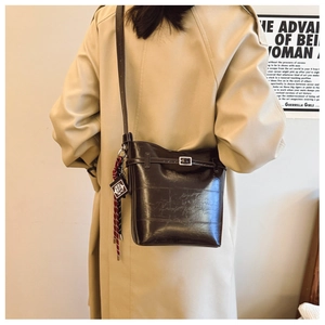 Detail of dark brown leather bucket bag with cross pendant and braided charm