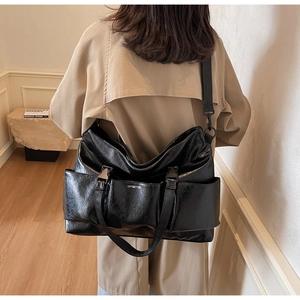 Detail view of large black glossy tote bag with double straps and functional side pockets