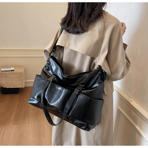 Detail of black tote bag featuring glossy crinkled texture and buckled utility pockets