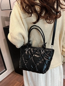 Sac seau matelassé noir avec détails argentés porté par un mannequin en extérieur