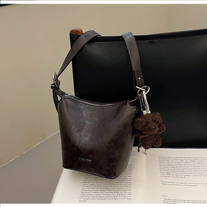 Detail of dark brown vintage bucket bag with plush bear charm on a retro book background