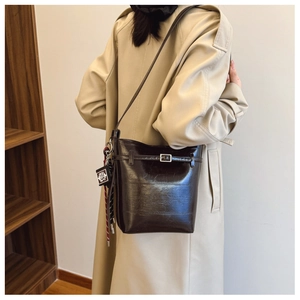 Detail of dark brown glossy bucket bag with metal buckle and decorative pendant