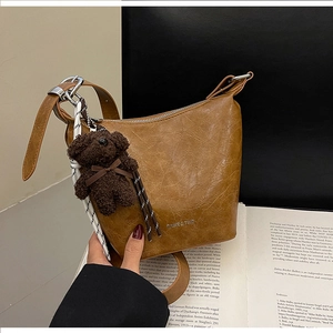 Detailed view of brown oil-wax leather bucket bag with logo and cute bear charm