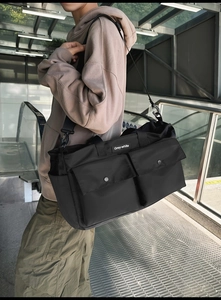Detail of black canvas tote bag showing two front snap pockets and industrial style straps