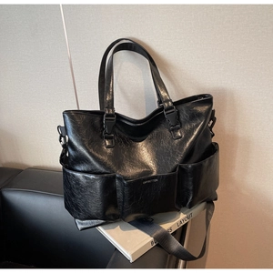 Detail of the glossy wrinkled texture and functional front pockets on a black tote bag