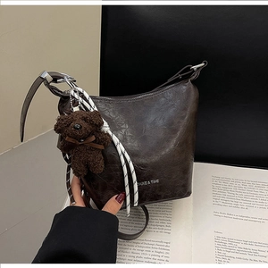 Detail of dark brown leather bucket bag with plush bear charm and silver zipper