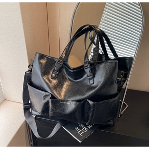 Detail of black tote bag featuring three front pockets and polished faux leather texture
