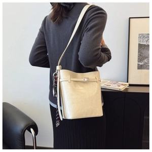 Detail of beige leather bucket bag with decorative tassel and adjustable strap on a model