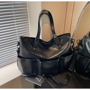 Detail of black faux leather tote bag showing multi-pocket design and adjustable strap
