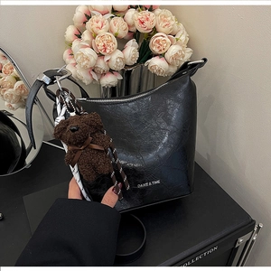 Detail of black vintage textured bucket bag with teddy bear charm and metal zipper