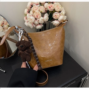 Detail of brown pleated bucket bag with plush bear charm and silver brand logo
