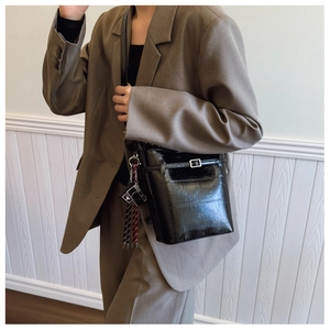 Close-up of black glossy bucket bag with silver buckle and camera charm detail