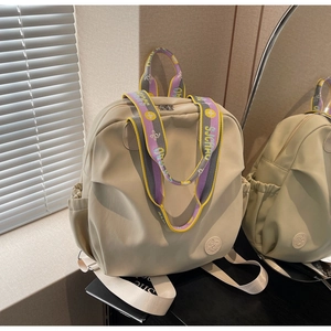 Detail of beige nylon backpack featuring a wide colorful embroidered shoulder strap