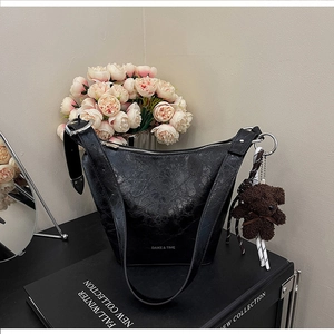 Detail of black faux leather bucket bag with silver hardware and plush bear charm