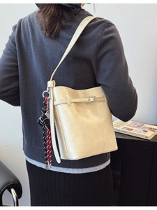 Minimalist cream bucket shoulder bag with adjustable strap and braided charm detail