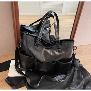 Detailed view of black oil wax leather tote bag featuring front pockets and metal logo