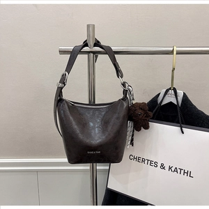 Detail view of brown leather bucket bag with wide strap and teddy bear charm on metal stand