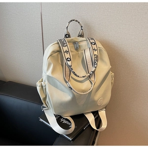 Detail view of cream nylon backpack with floral patterned wide straps on a leather sofa