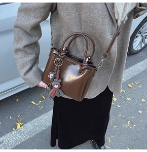 Détail d'un sac seau marron foncé brillant avec breloque ours en peluche et poignées