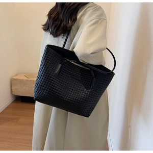 Detail of the intricate black woven texture and slim leather strap on a large tote bag