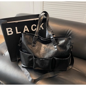 Detail of black multi-pocket tote bag in glossy distressed leather with buckle straps
