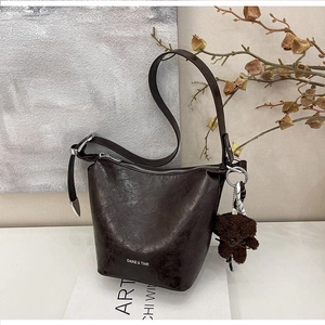 Detail of dark brown leather bucket bag featuring silver hardware and plush bear charm