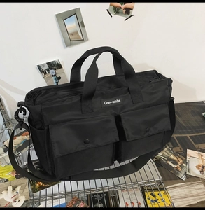 Detail of black canvas tote bag showing double front snap pockets and adjustable strap