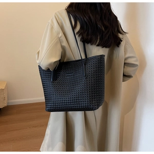 Detail of the black woven tote bag showing its intricate checkerboard texture and dual straps