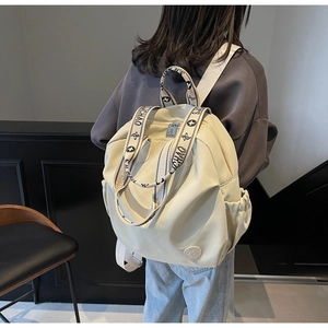 Detail of cream nylon backpack featuring contrast lettered straps and side drawstring pockets