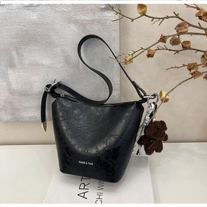 Detail of black pleated bucket bag with wide strap and brown plush bear charm accessory