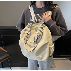 Detail of cream nylon backpack showing brand leather patch and dual metal zipper closure