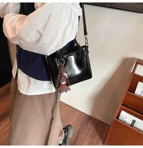 Detalle de bolso tote negro brillante con un colgante de oso pardo y letras blancas
