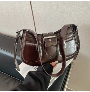 Detail of dark brown retro underarm bag with metal buckle strap and punk-style zippers