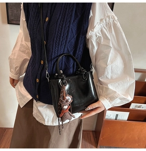 Détail du sac seau noir brillant avec charm ours et bandoulière en cuir élégante