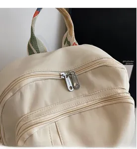 Close-up of dual metal zippers and red-green woven handle on a beige canvas backpack