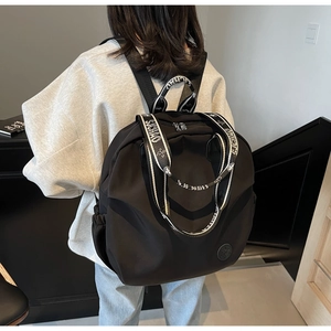 Detail of black nylon backpack featuring woven handles and stylish logo on woman's back