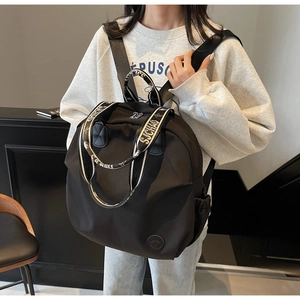 Close-up of black nylon backpack featuring letter-pattern straps and side drawstring pocket