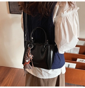 Détail du sac cabas en cuir verni noir avec charme d'ours et bandoulière réglable