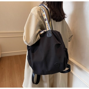 Detail of black nylon backpack with colorful jacquard strap worn by a woman in trench coat
