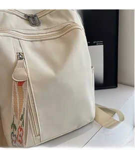 Detail of beige nylon backpack showing soft textured fabric and floral woven strap