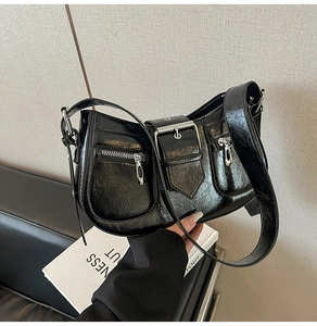 Close-up of black glossy leather underarm bag with zippers and metal buckle