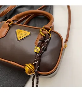 Close-up of dark brown leather Boston bag featuring gold logo charm and detailed texture