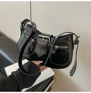 Detail of black glossy saddle bag featuring double zipper pockets and silver metal buckle