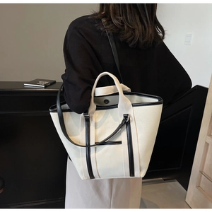 Detail of canvas tote bag with black leather trim, showing dual handles and shoulder strap
