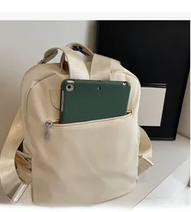 Close-up of beige nylon backpack featuring front zipper pocket and embroidered strap details