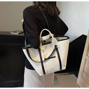 Close-up of contrast canvas tote bag featuring black leather trim and dual straps