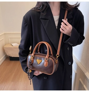 Detail of a dark brown bowling handbag with a golden triangle plaque and crossbody strap