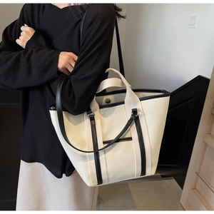 Detail of canvas tote bag with black leather trim and magnetic buckle on model